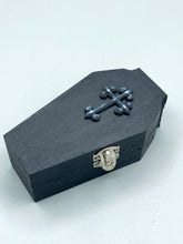 Load image into Gallery viewer, This unique vintage-inspired ring box is perfect for storing your jewelry and other special items. The wood coffin design is accented with a detailed black silver cross. The interior is lined with a skull fabric and a large dark red rose, adding a spooky yet elegant flair.
