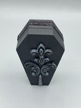Load image into Gallery viewer, This vintage-inspired coffin ring box will make a spooky yet cute addition to any jewelry collection. The sleek black box has eye-catching black and gray embellishments, while the interior is beautifully decorated with a vivid turquoise blue fabric and a highly detailed black and silver cross with dark red roses. Function and style meet with this unique and stylish piece.
