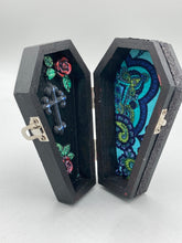 Load image into Gallery viewer, This vintage-inspired coffin ring box will make a spooky yet cute addition to any jewelry collection. The sleek black box has eye-catching black and gray embellishments, while the interior is beautifully decorated with a vivid turquoise blue fabric and a highly detailed black and silver cross with dark red roses. Function and style meet with this unique and stylish piece.
