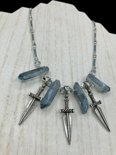This elegant and dark necklace features shimmering light silver and gray glass beads of varying sizes and shapes for texture and dimension. The necklace is finished with blue luster crystal stone nuggets and nickel-free dagger pendants, creating a beautiful draping effect. Measurements:   Necklace is 17”adjustable up to 19