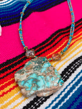 Load image into Gallery viewer, This vibrant and striking double strand necklace features a combination of glass beads in blue and green shades of turquoise, gold and champagne. The two delicate strands are accented with a gold-tone flower-shaped bead, a howlite stone chip dyed in turquoise, and shimmery, cross-faceted champagne-colored glass beads to complete the dramatic look.  Measurements:   Necklace is 17” and can be adjusted up to 19"
