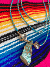 Load image into Gallery viewer, This vibrant and enchanting Southwestern Style inspired necklace is comprised of three strands. The first two feature a mix of blue and green turquoise and gold glass beads, while the longest strand features a howlite stone chip dyed turquoise and shimmery cross faceted champaign color glass beads for a dramatic look.  Measurements: The Necklace is 16” and can be adjusted up to 18" 
