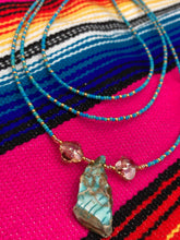 Load image into Gallery viewer, This vibrant and enchanting Southwestern Style inspired necklace is comprised of three strands. The first two feature a mix of blue and green turquoise and gold glass beads, while the longest strand features a howlite stone chip dyed turquoise and shimmery cross faceted champaign color glass beads for a dramatic look.  Measurements: The Necklace is 16” and can be adjusted up to 18" 
